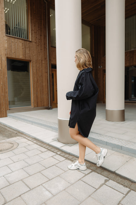 Woman in a black dress standing near columns in an outdoor setting