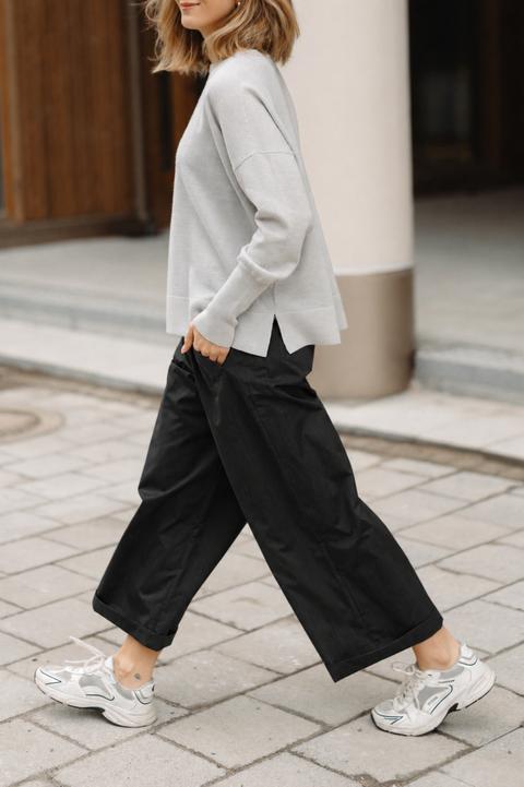 Person wearing a gray sweater and black pants on a city street.