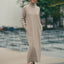 Woman wearing a long beige dress with a turtleneck standing outdoors.