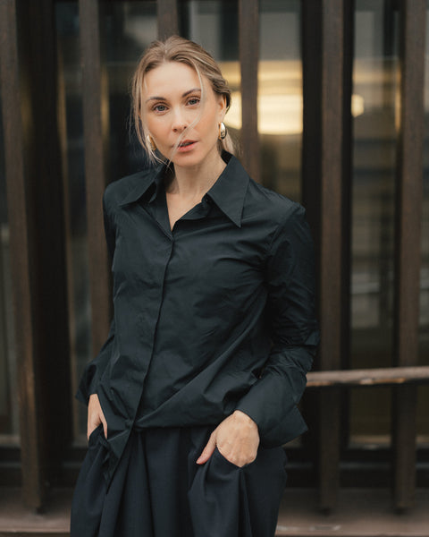 Woman wearing a black shirt and skirt standing in front of a building.
